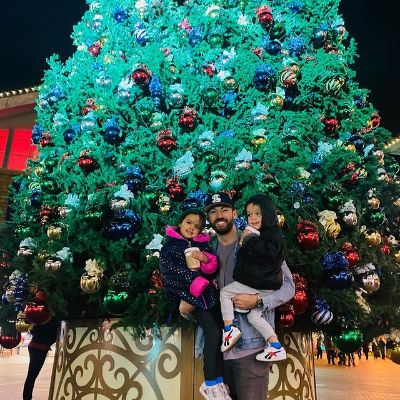 He is carrying both his babies and standing in front of a huge Christmas tree.